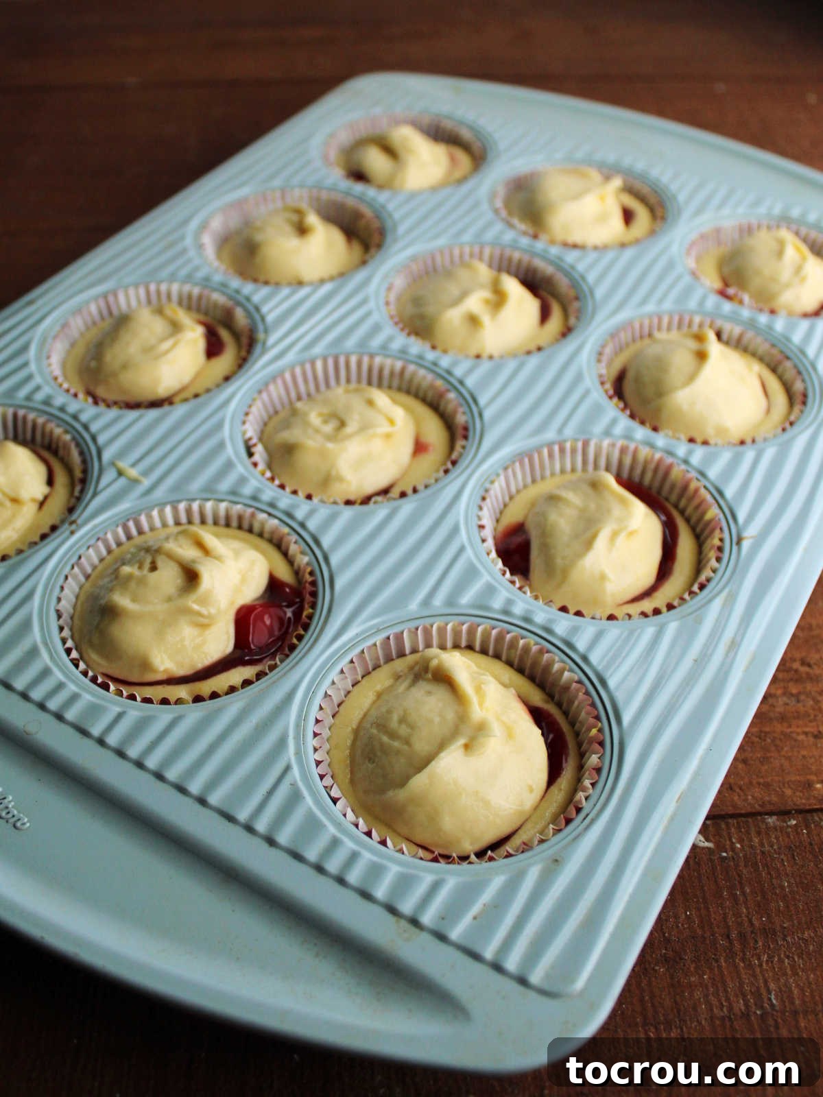 Cupcake bases topped with cherry pie filling and more cupcake batter ready to go back in the oven.