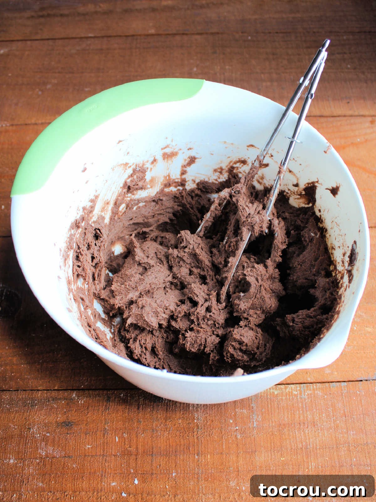 Mixing bowl with thick chocolate gooey butter cookie dough and mixer beaters inside.