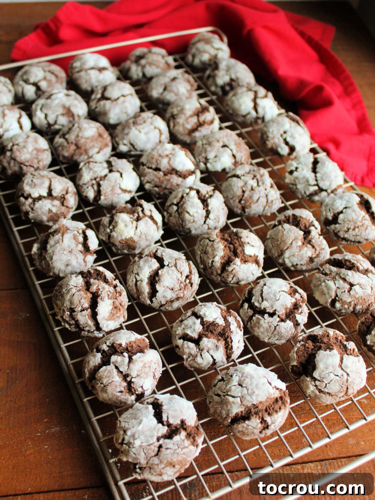 Baked chocolate cookies with powdered sugar exterior cooling on wire rack.
