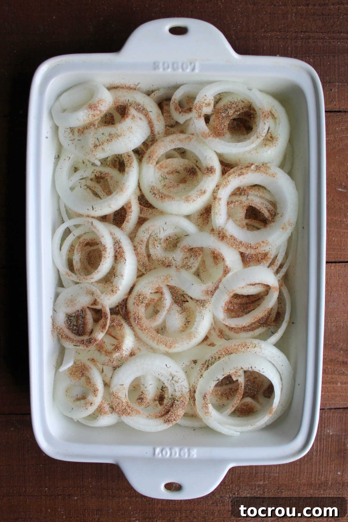 Seasonings sprinkled over onion rings in baking pan.