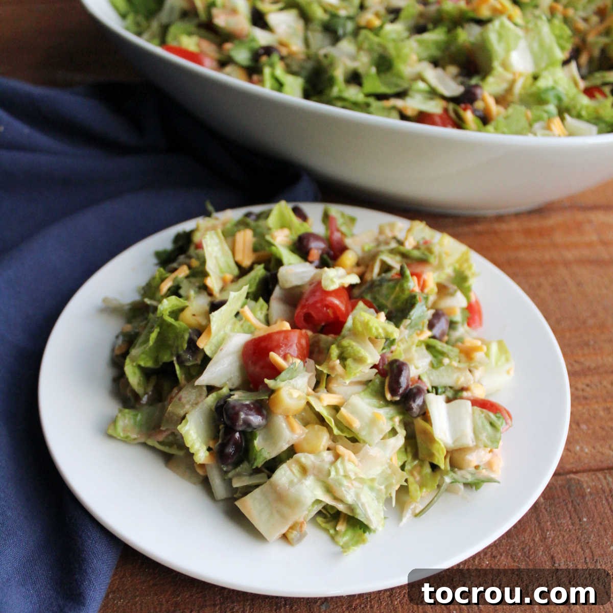 Close up plate of cowboy salad showing lettuce with tomatoes, corn, black beans, cheese, cilantro, and creamy salad dressing.