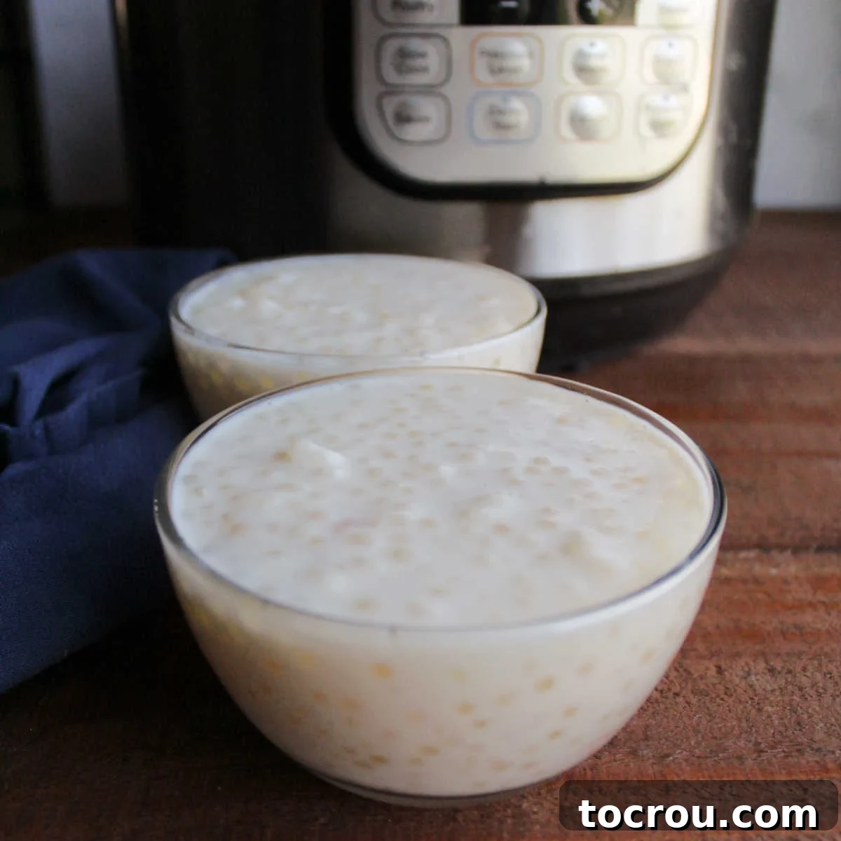 Two small glass bowls filled with rich vanilla tapioca pudding, perfectly cooked, resting in front of an Instant Pot, symbolizing ease and homemade goodness.