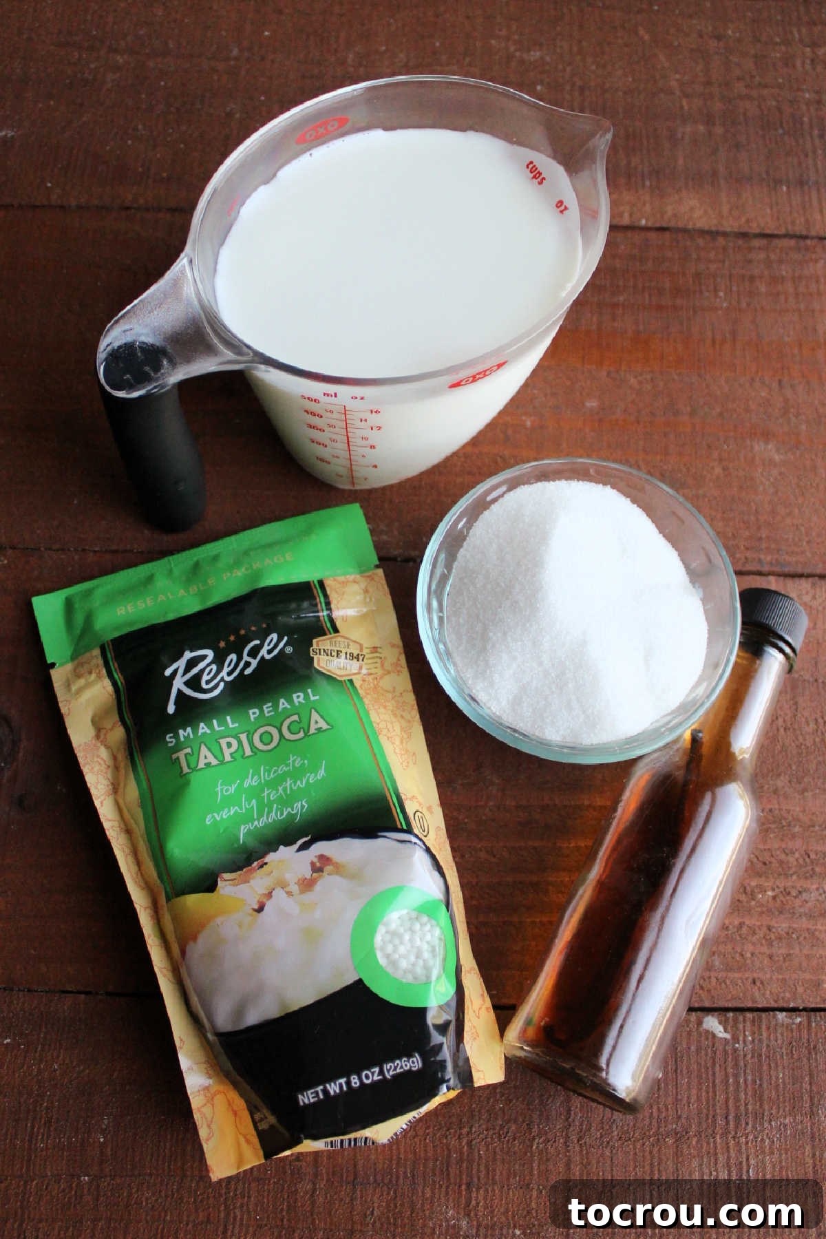 Essential ingredients for tapioca pudding laid out: fresh milk, granulated sugar, pure vanilla extract, and small tapioca pearls, ready for preparation.