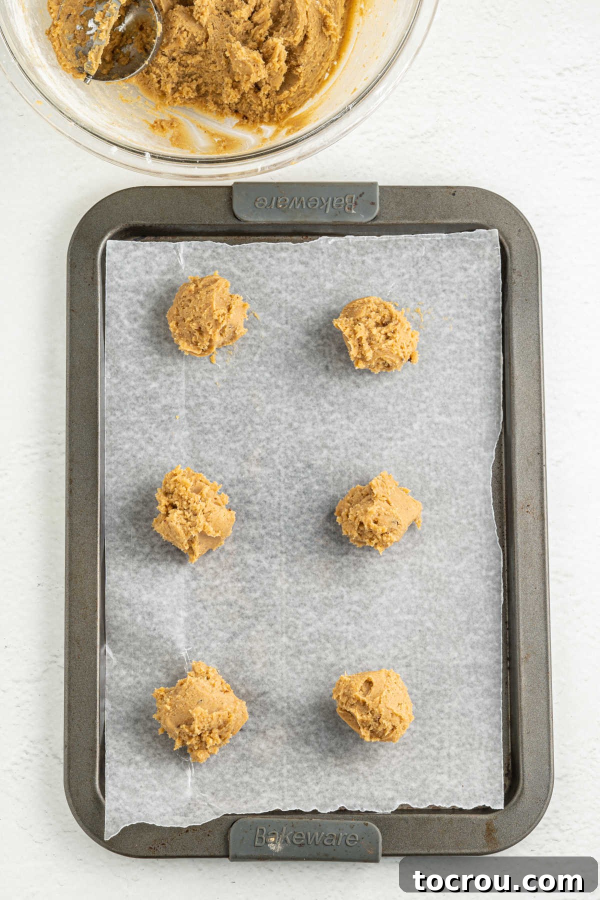 Scoops of chai cookie dough on a parchment lined cookie sheet, ready to bake.