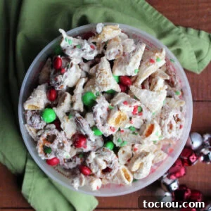 Close up of container of white chocolate Christmas snack mix with bugles, pretzels, peanuts, sprinkles and M&Ms.