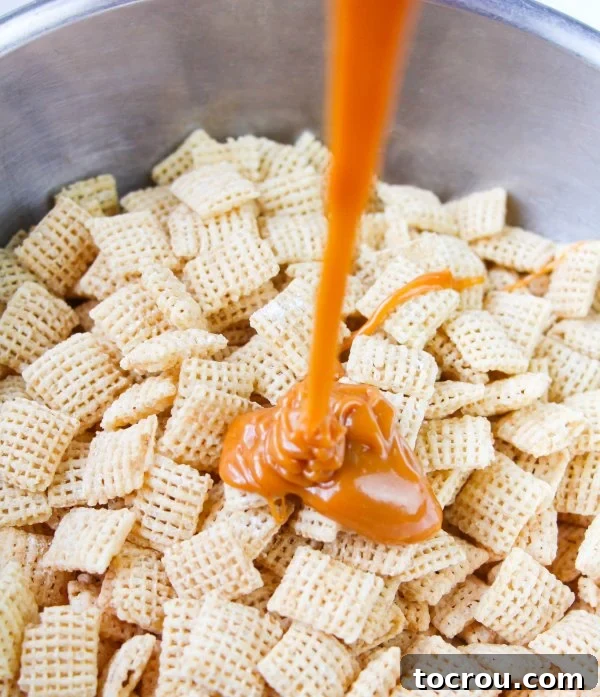 Irresistible Caramel Puppy Chow 3 A close-up shot of melted caramel being poured over a bowl of Chex cereal, showing the glossy coating process.