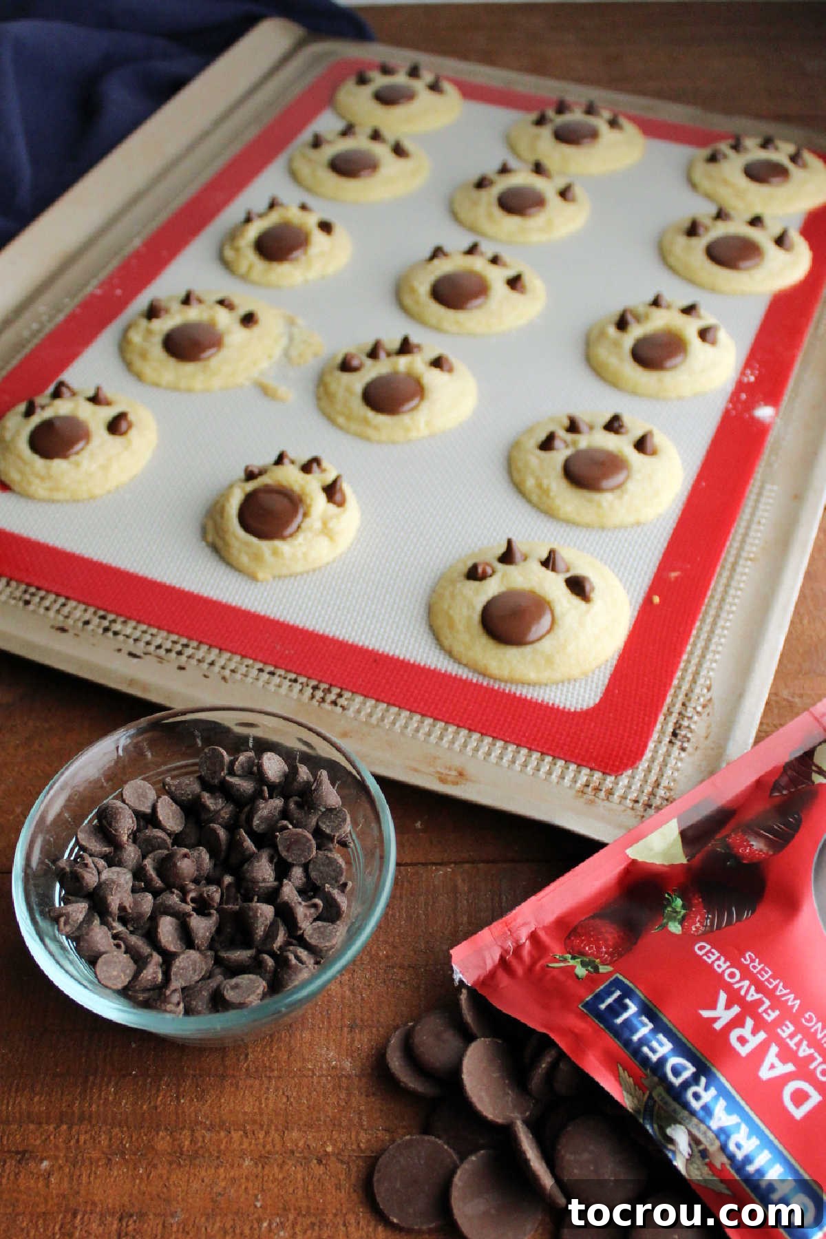 Sweet Vanilla Paw Delights 7 The step-by-step process of carefully pressing a larger chocolate wafer and four smaller chocolate chips into freshly baked, still-warm vanilla sugar cookies to artfully form charming paw print designs.