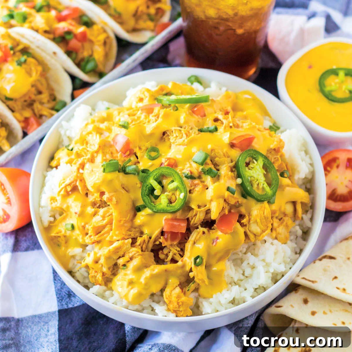 Slow Cooker Queso Chicken Rice Bowl A vibrant bowl of rice generously topped with creamy queso chicken, fresh herbs, juicy diced tomatoes, and thinly sliced jalapeños, ready to be enjoyed.