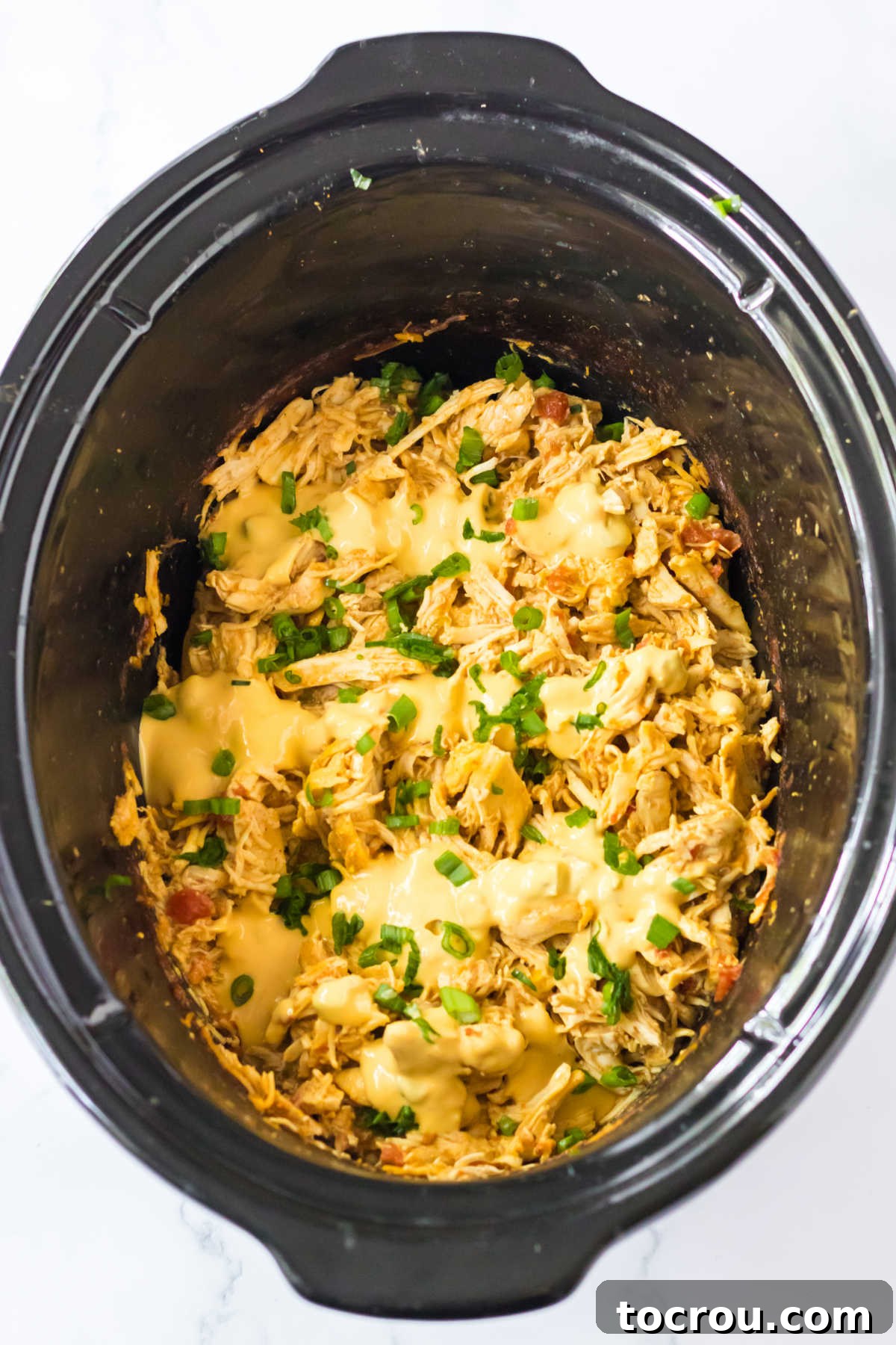 Shredded Queso Chicken Close-up of shredded chicken, perfectly cooked and topped with an extra dollop of creamy queso, ready for serving.