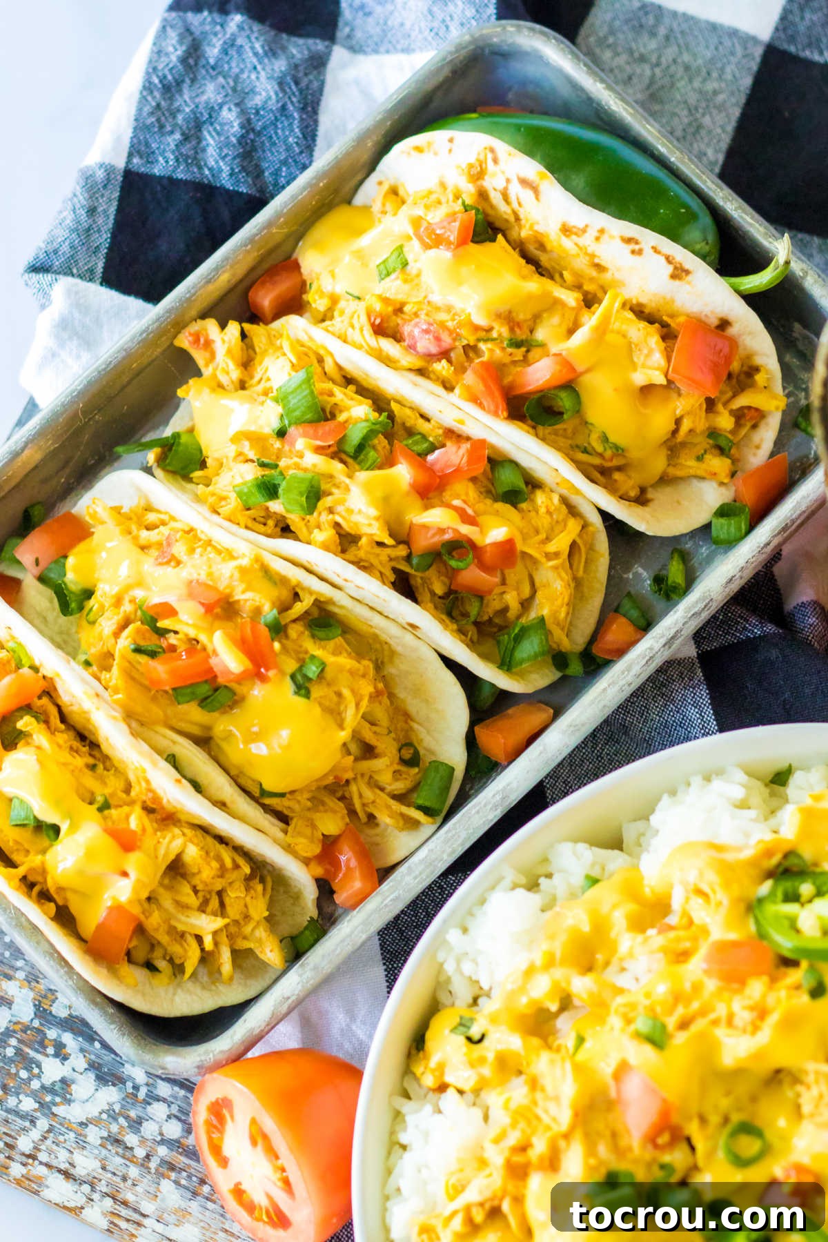 Queso Chicken Tacos A rustic wooden tray laden with several mouth-watering queso chicken tacos, generously topped with extra queso, fresh cilantro, and finely chopped tomatoes.