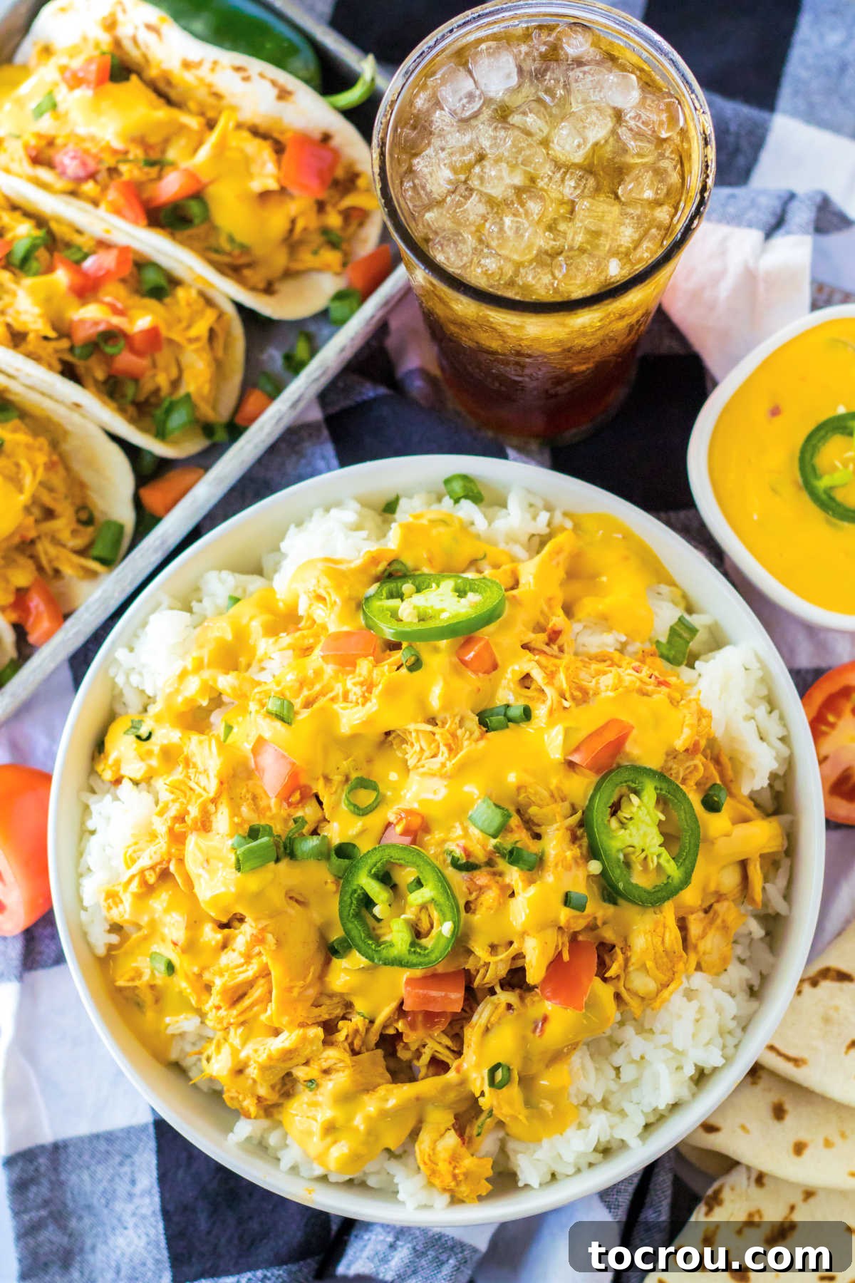 Queso Chicken Meal Spread A delightful meal scene featuring a hearty queso chicken and rice bowl alongside a refreshing glass of iced tea, with more tempting queso chicken tacos artfully blurred in the background.
