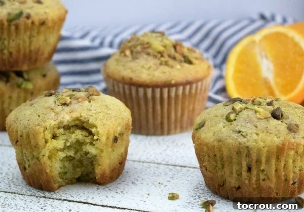 Ready-to-eat orange pistachio muffins with an orange half and pistachio pieces, showcasing their vibrant color and texture.