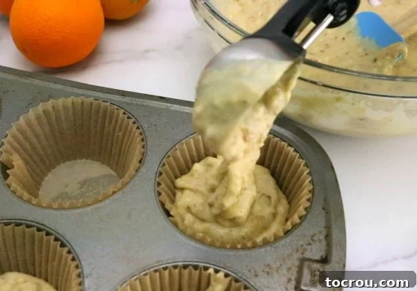 Using an ice cream scoop to transfer orange pistachio muffin batter into cupcake liners, showing an efficient baking technique.