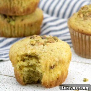 Orange pistachio muffin with bite missing, showing soft interior with bits of pistachio on top.