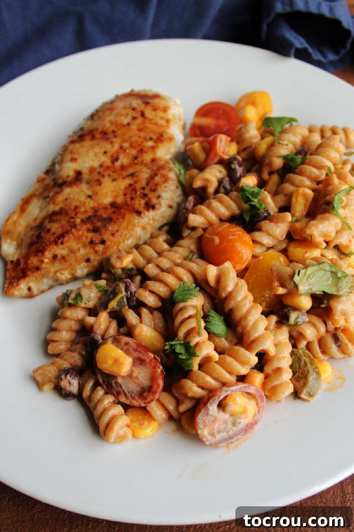 Enchilada Macaroni Salad Paired with Grilled Chicken A close-up shot of enchilada macaroni salad served alongside succulent grilled chipotle chicken on a dinner plate, illustrating a perfectly balanced and appetizing meal.