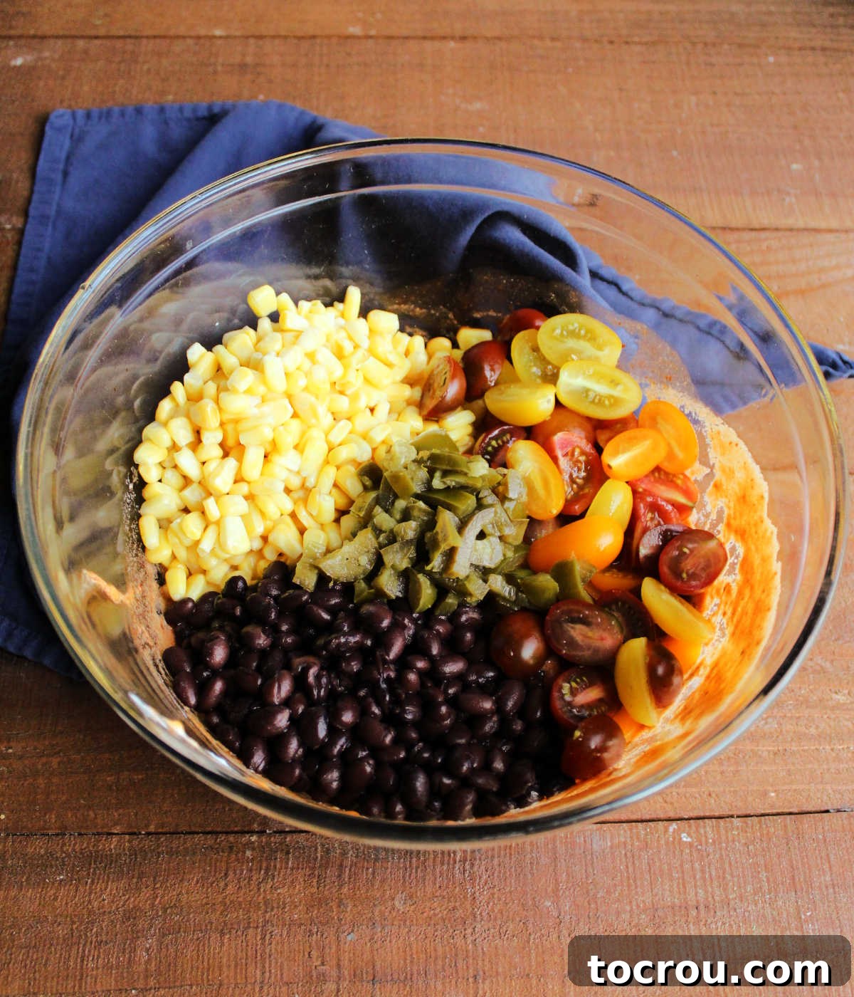 Combining Ingredients for Enchilada Pasta Salad A bowl filled with a colorful mix of corn, black beans, halved cherry tomatoes, and diced pickled jalapenos, all coated in the creamy enchilada dressing, illustrating the perfect blend of ingredients for the pasta salad.