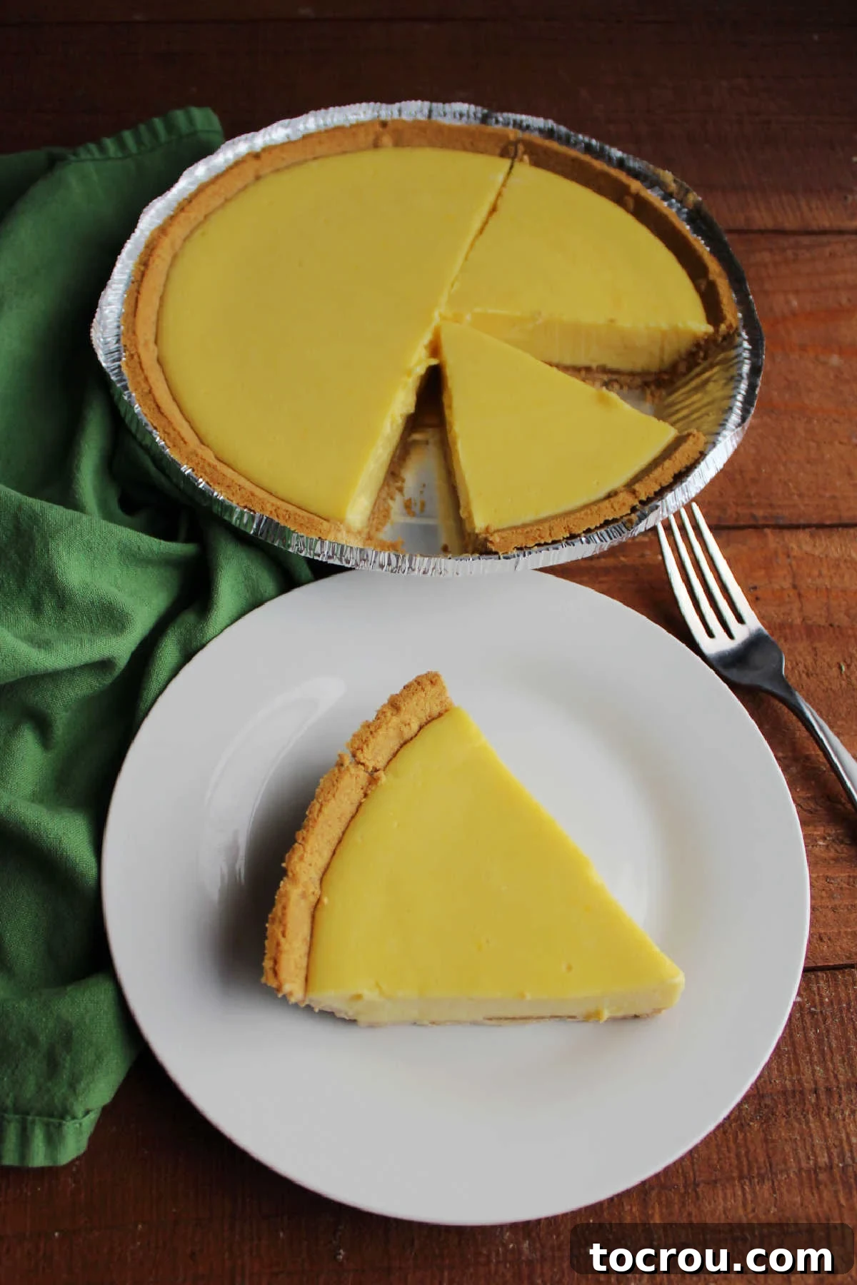 A perfectly portioned slice of key lime pie on a small white dessert plate, with the remaining pie visible in the background, highlighting its inviting golden crust and smooth lime filling.