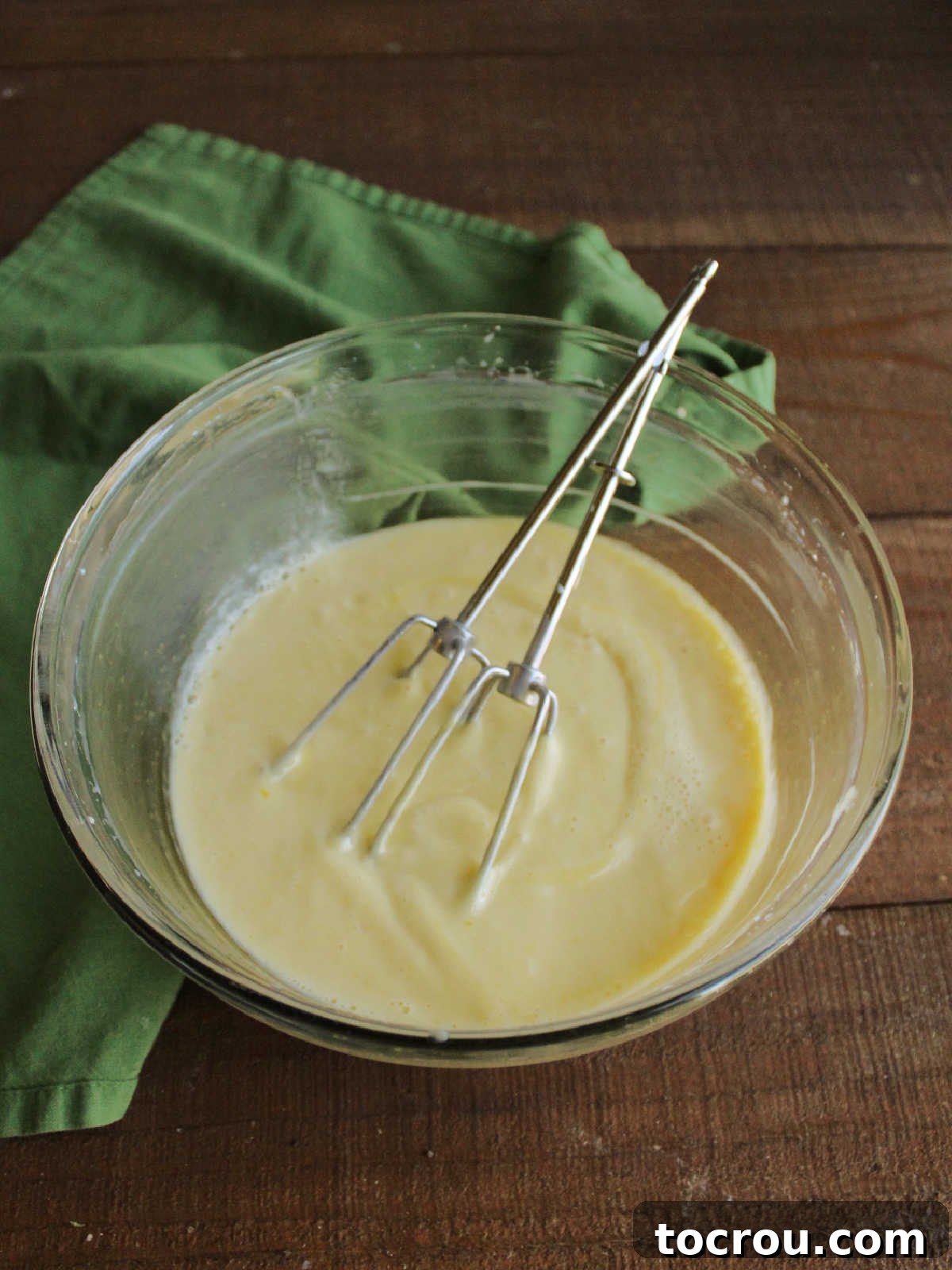 A mixing bowl filled with the pale green, smooth key lime pie filling, with mixer beaters resting within, indicating it's perfectly prepared and ready to be poured into the pie crust.