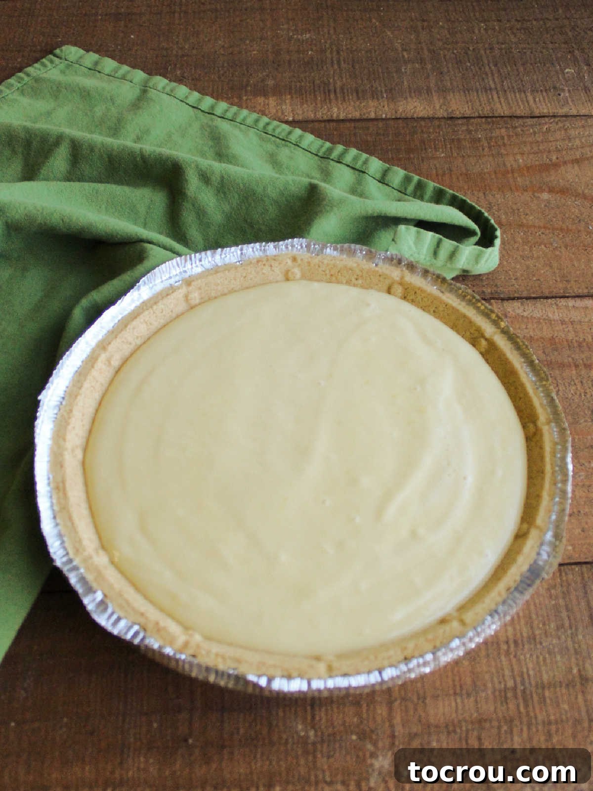 An unbaked key lime pie, with its creamy pale green filling perfectly smoothed into a graham cracker crust, sitting on a baking sheet, ready for the oven.