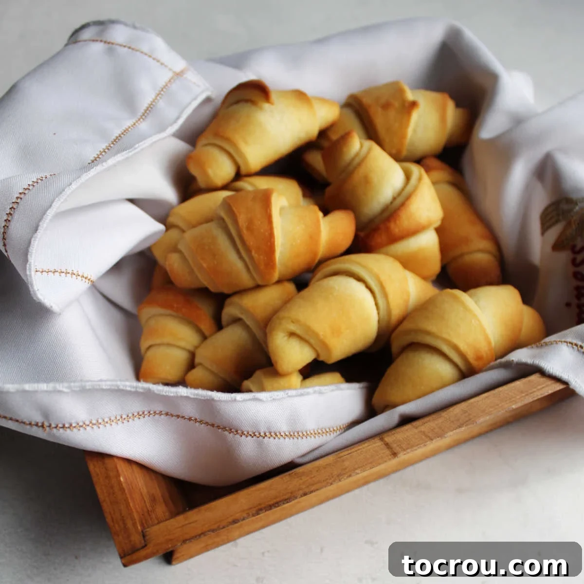 Basket of fresh homemade crescent rolls with buttery golden brown exterior and classic horn shape. 