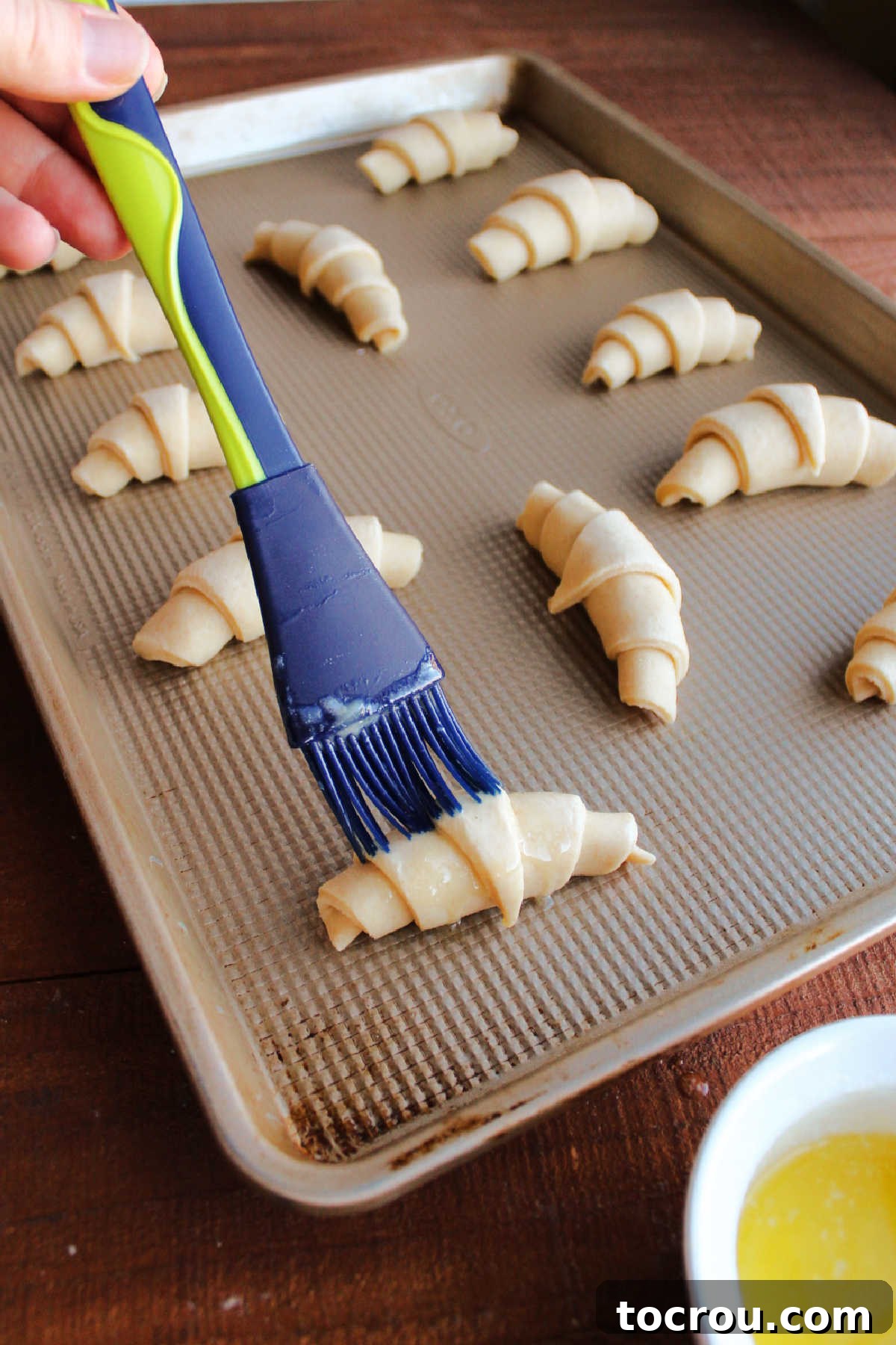 Brushing proofed crescent rolls with butter before they go into the oven.