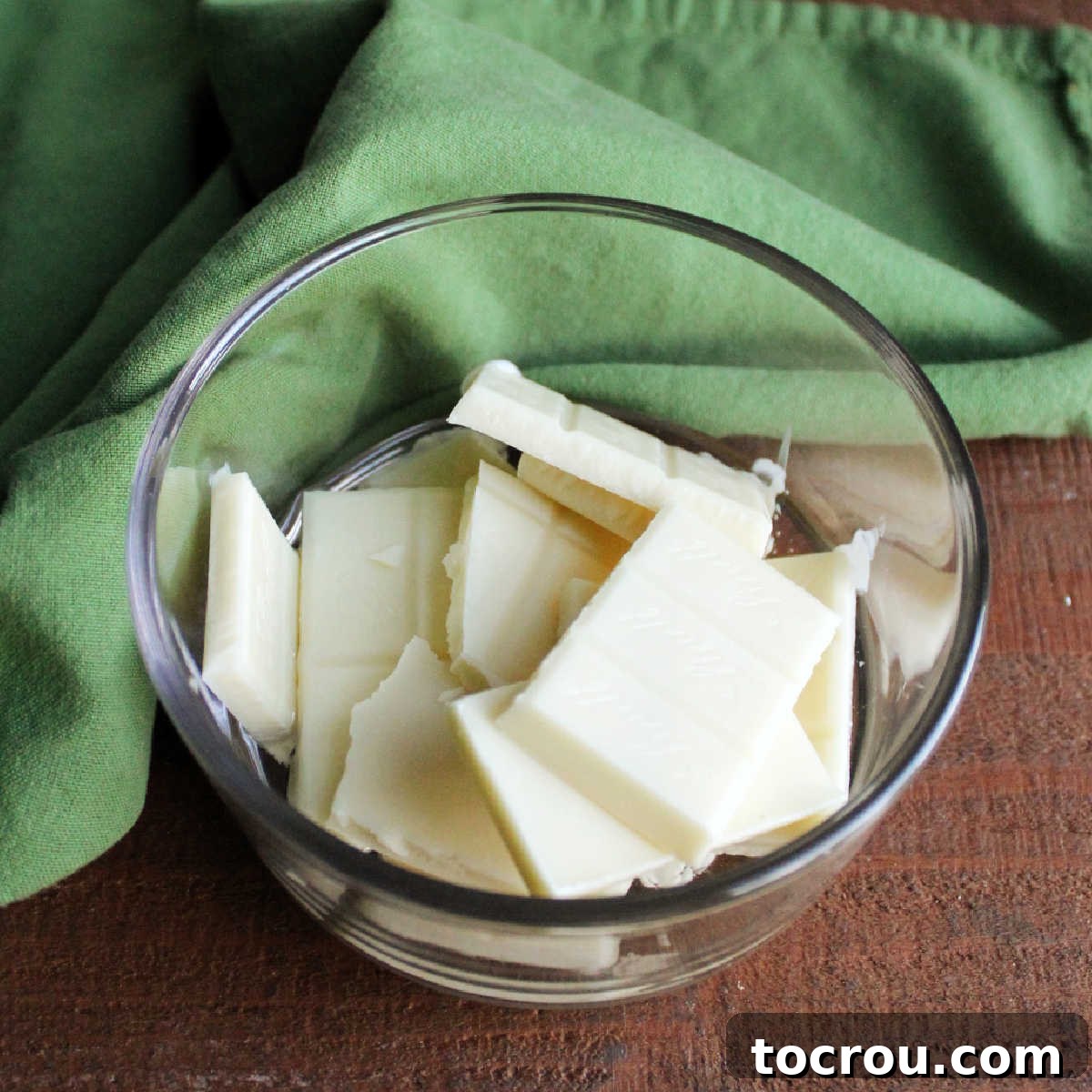 DIY Unicorn Rainbow Glaze 5 Broken pieces of white chocolate bar and coconut oil in small glass container.