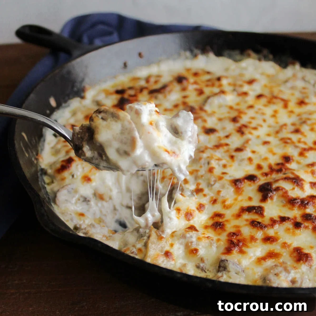 Creamy Baked Sausage Mushroom Dip 2 A spoon lifts a generous scoop of hot, gooey stuffed mushroom dip, revealing melted cheese, crumbled sausage, and tender mushroom pieces.