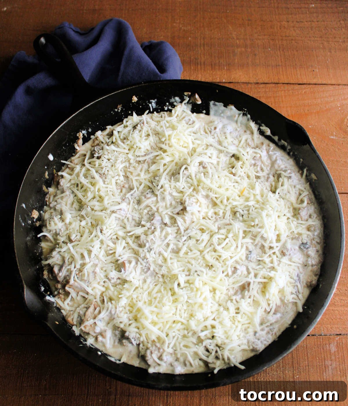 Creamy Baked Sausage Mushroom Dip 7 A cast iron skillet of creamy stuffed mushroom dip, generously topped with shredded mozzarella cheese, ready to be baked in the oven.