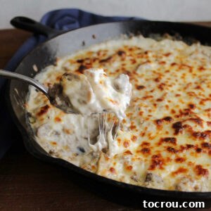 Creamy Baked Sausage Mushroom Dip 10 Spoon lifting out cheesy stuffed mushroom dip with bits of sausage and melted cheese visible.