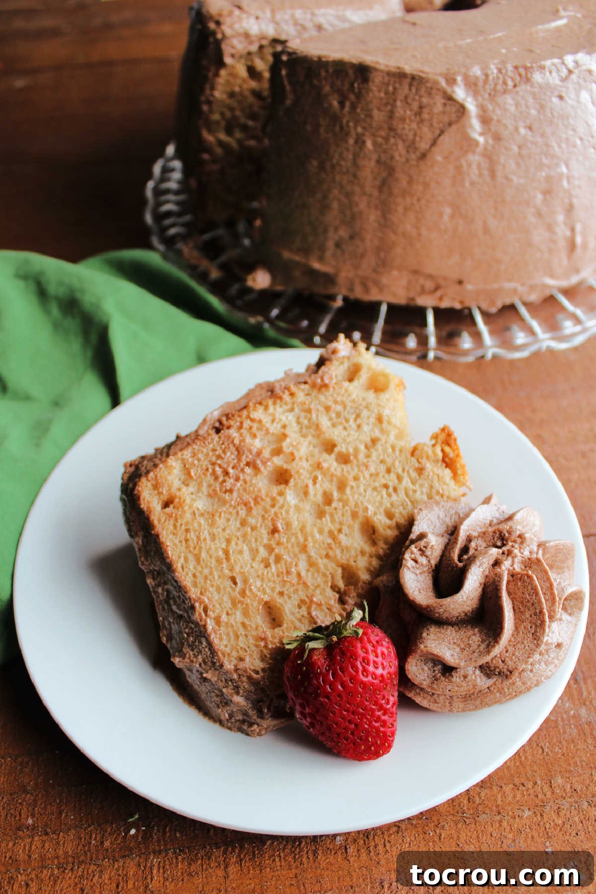 Slice of coffee angel food cake served with an extra swirl of mocha frosting and a fresh strawberry with the remaining cake in the background.