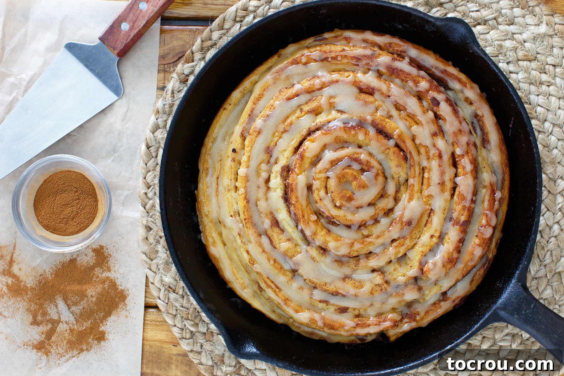 Cozy Skillet Pumpkin Spice Cinnamon Rolls 2 Cast iron skillet with a large, golden-brown pumpkin spice cinnamon roll cake, generously topped with maple brown butter glaze.