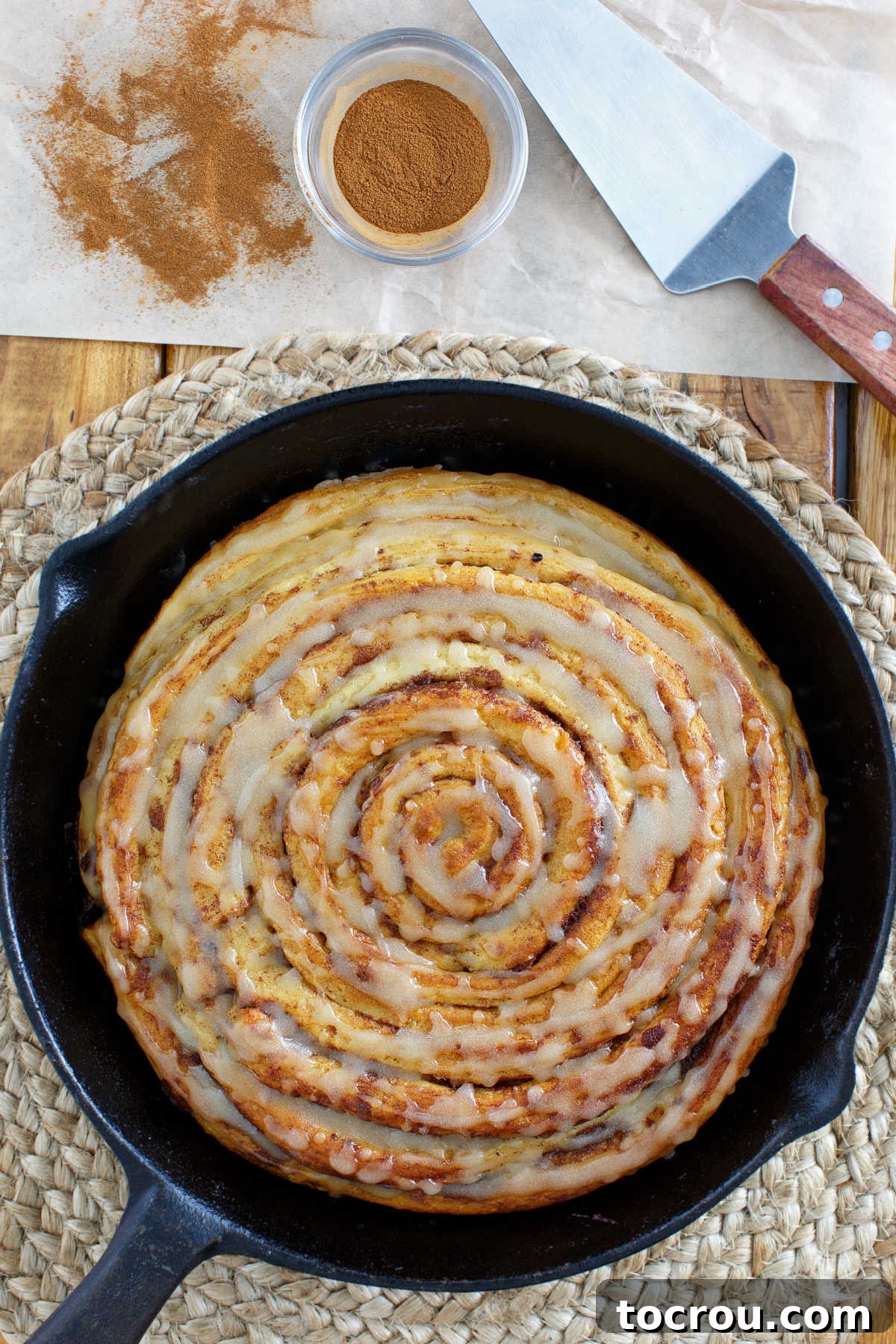 Cozy Skillet Pumpkin Spice Cinnamon Rolls 3 Close-up of a giant pumpkin spice cinnamon roll in a cast iron skillet, generously drizzled with a shiny maple browned butter glaze.