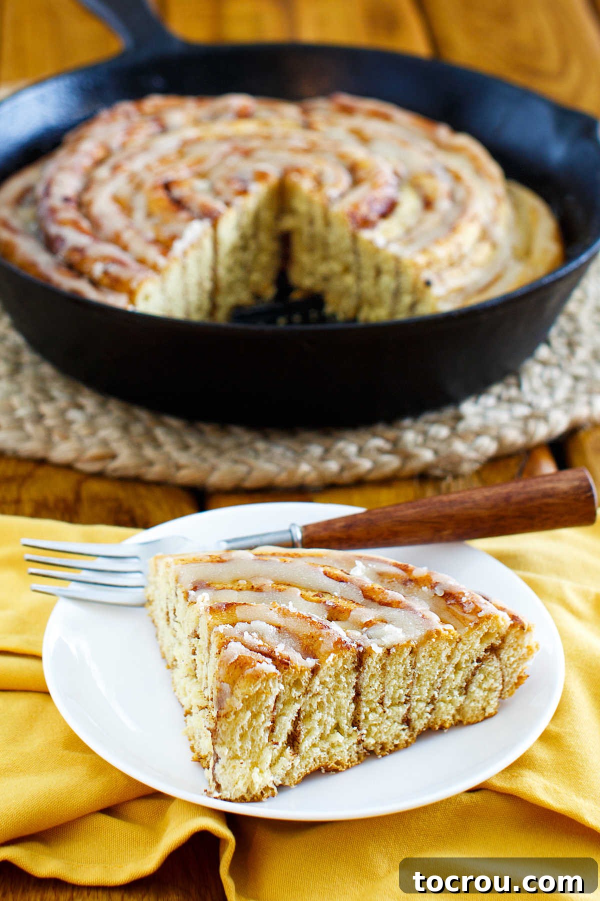 Cozy Skillet Pumpkin Spice Cinnamon Rolls 4 A freshly cut slice of pumpkin spice skillet cinnamon roll served on a plate, with the remaining roll visible in the cast iron skillet in the background.