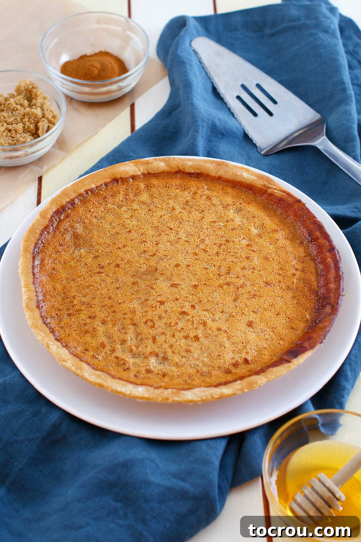 Enjoy this honey sweetened twist on a chess pie. With a kiss of lemon, honey richness and lots of chess pie goodness, it is a perfect treat for almost any occasion! Freshly baked honey chess pie with golden brown top, ready to be served.