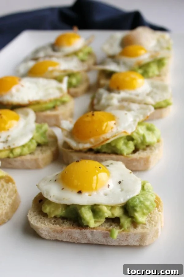 Toasted baguette slices topped with creamy avocado and perfectly fried quail eggs, arranged for serving.