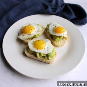 Three avocado and quail egg crostini served on a small plate.