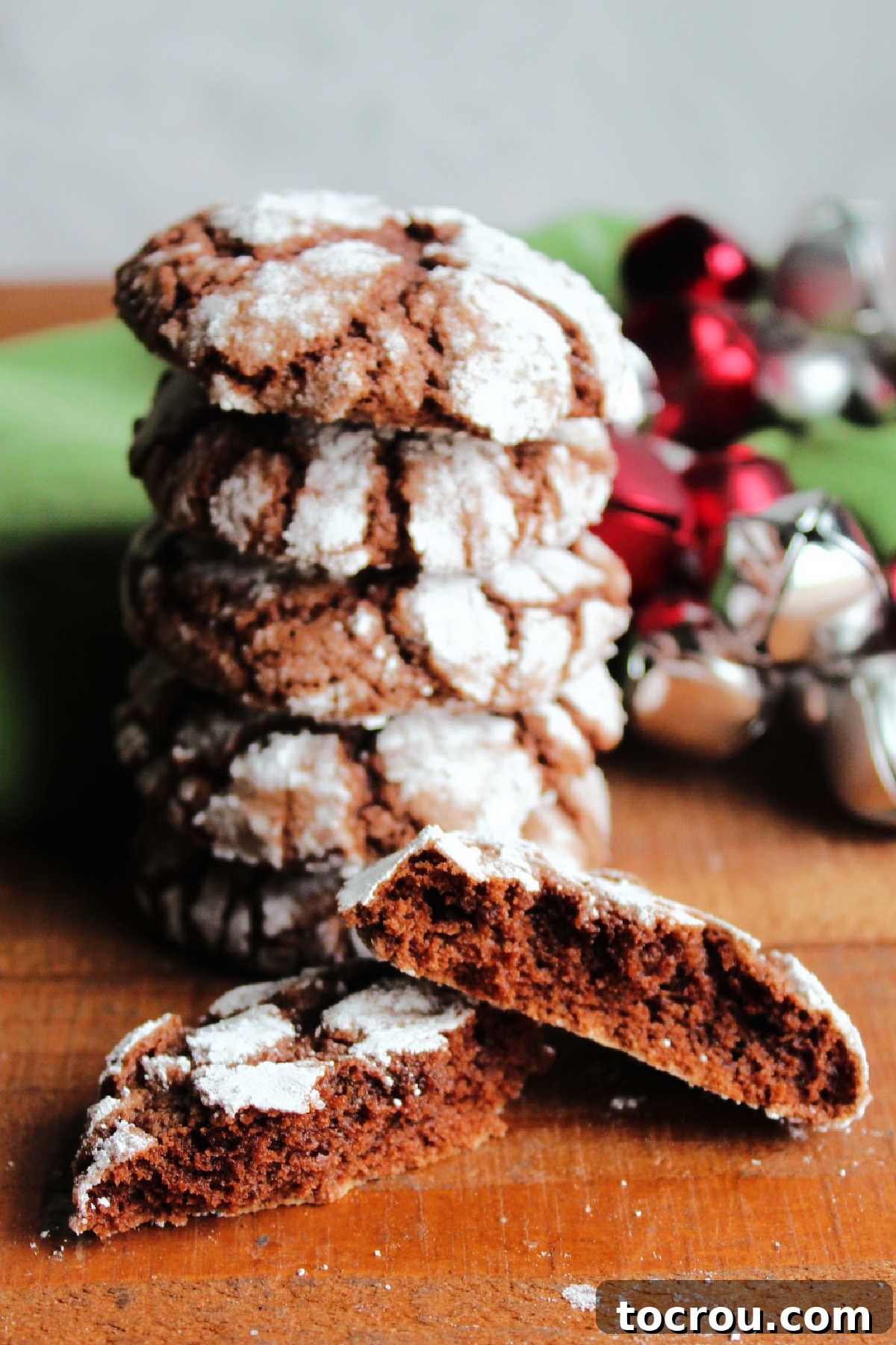 Chocolate crinkle cookie broken in half showing soft interior and crackled exterior in front of stack of cookies.