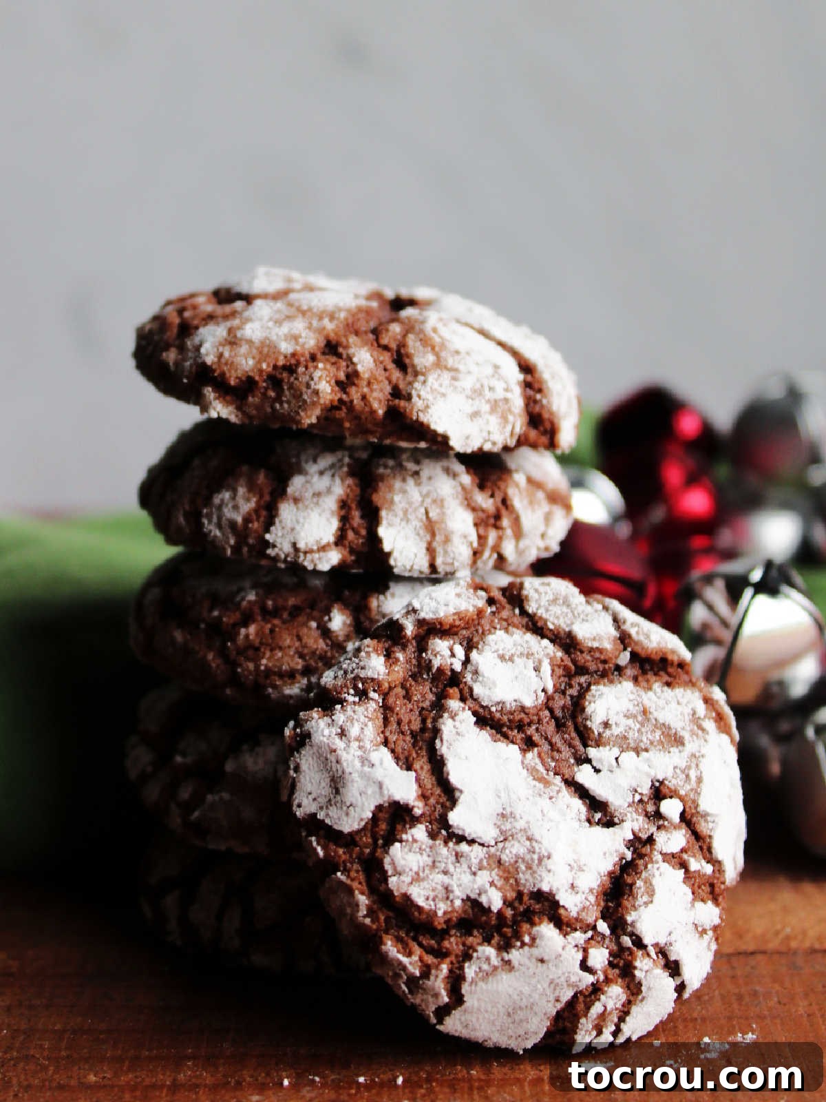Chocolate crinkle cookie with powdered sugar exterior leaned up against a stack of more cookies.