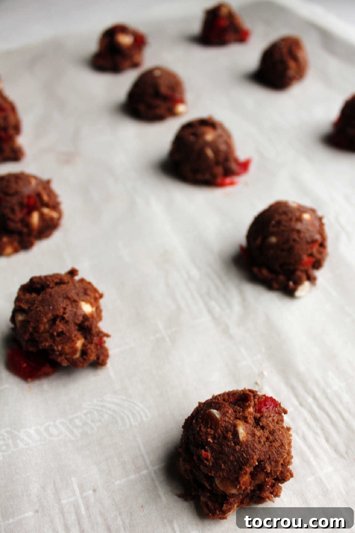 Cookie dough ready for baking. Perfectly scooped balls of chocolate cherry chip cookie dough arranged on a parchment-lined baking sheet, awaiting the oven.