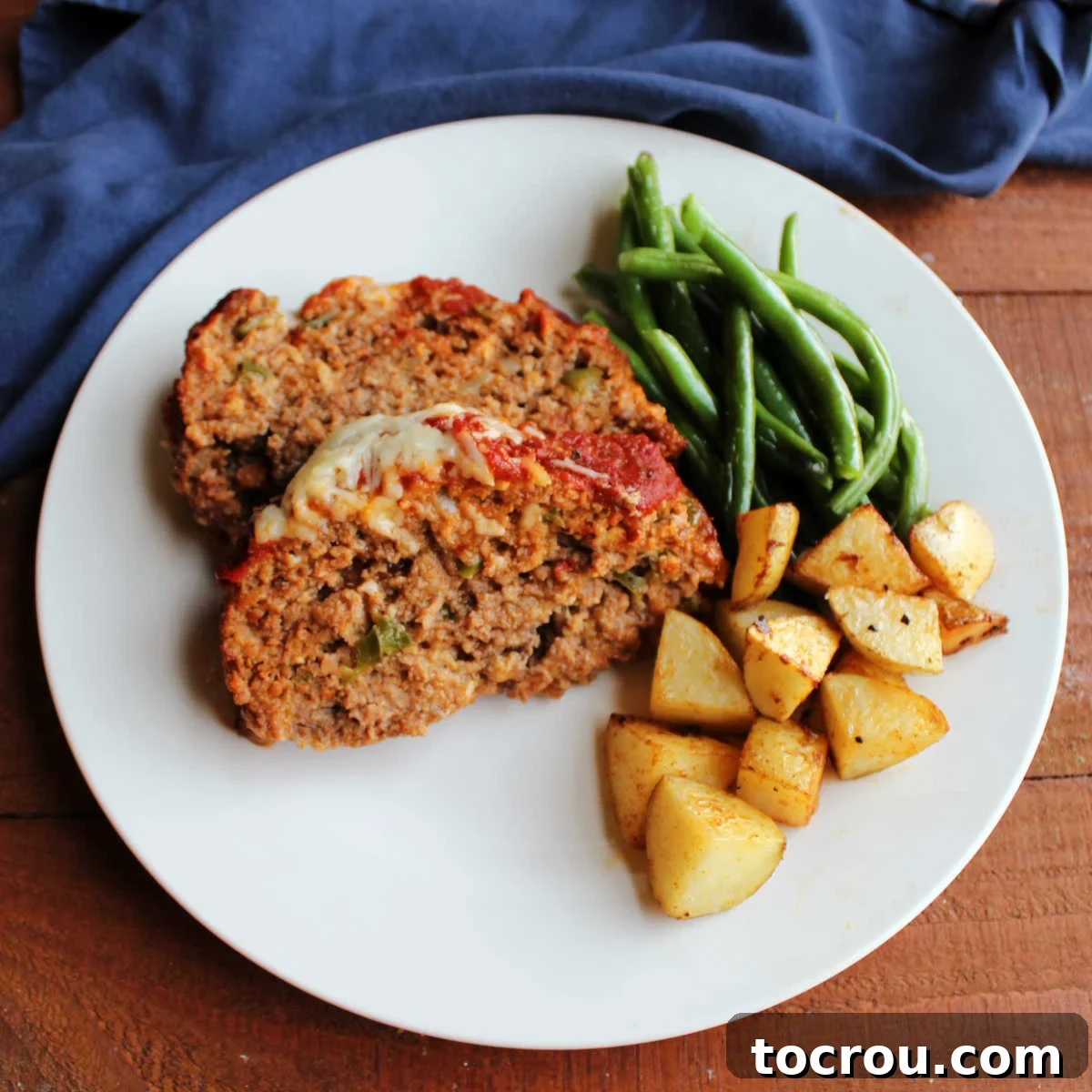 Dinner plate with two slices of Italian sausage meatloaf, roasted potatoes, and roasted green beans. A delicious, hearty meal ready to be served.