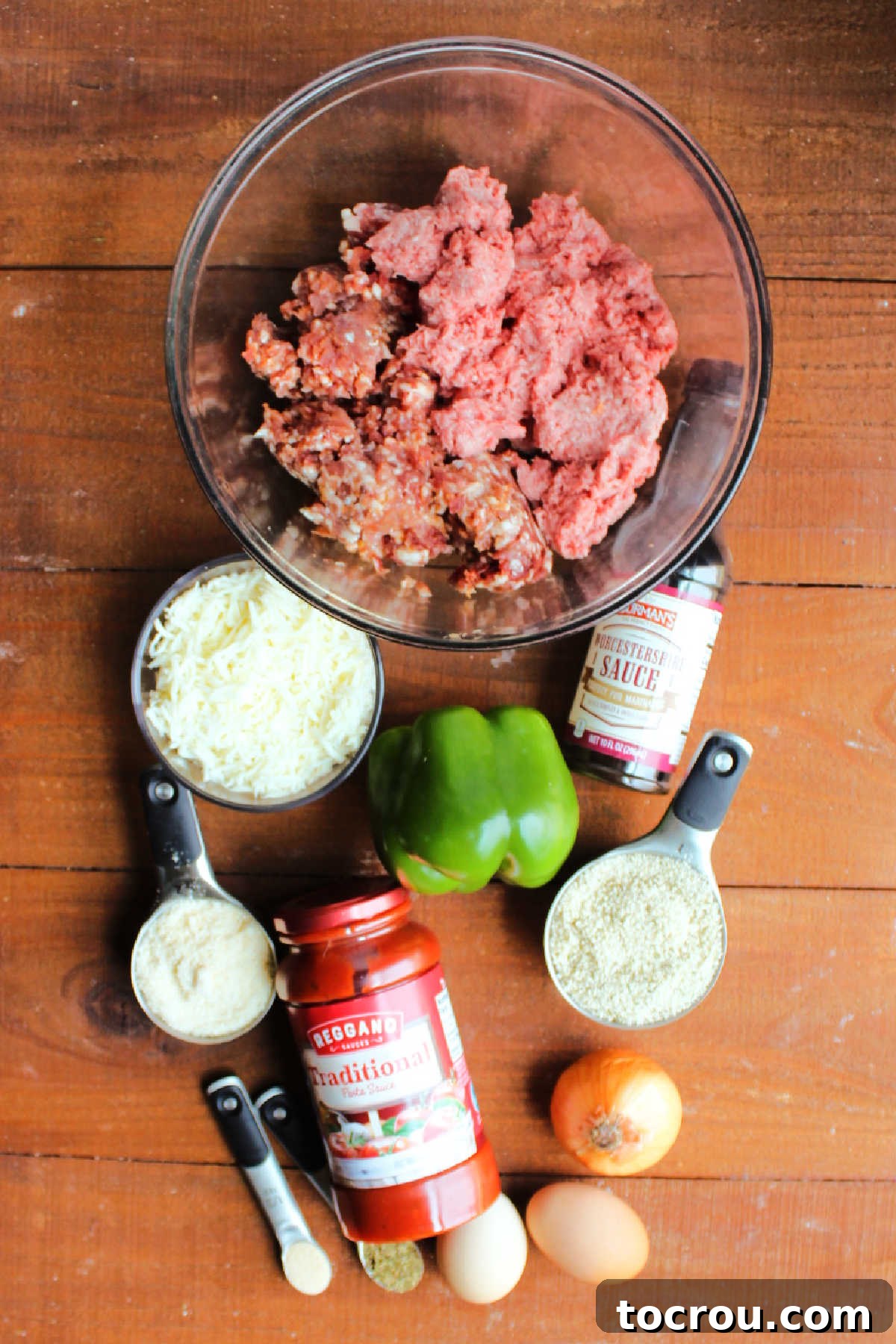 Ingredients for Italian meatloaf laid out on a counter, including ground beef, Italian sausage, bell pepper, onion, eggs, bread crumbs, marinara sauce, and Worcestershire sauce, ready for mixing.
