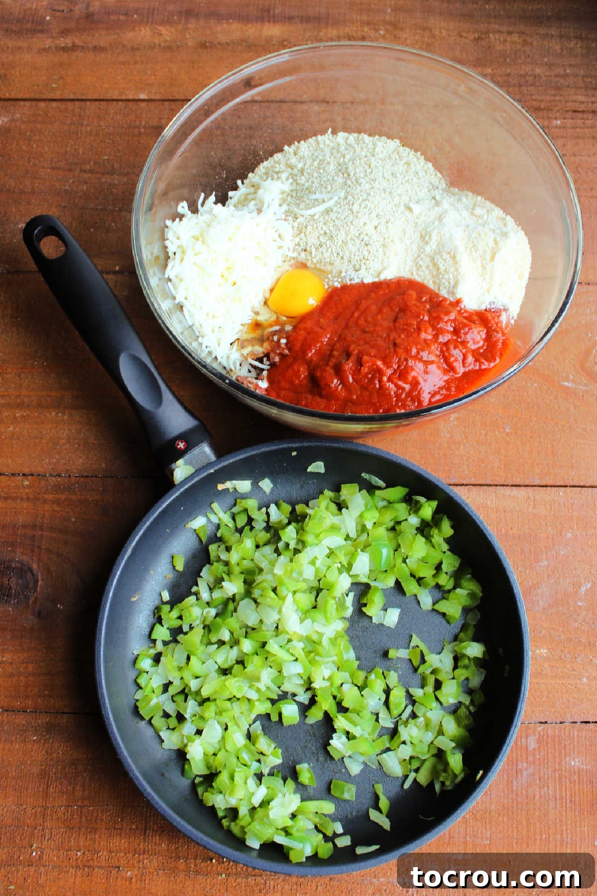 Bowl of meat topped with bread crumbs, eggs, cheese, and marinara sauce next to a skillet with sautéed onions and pepper, ready to be mixed together for the Italian meatloaf.