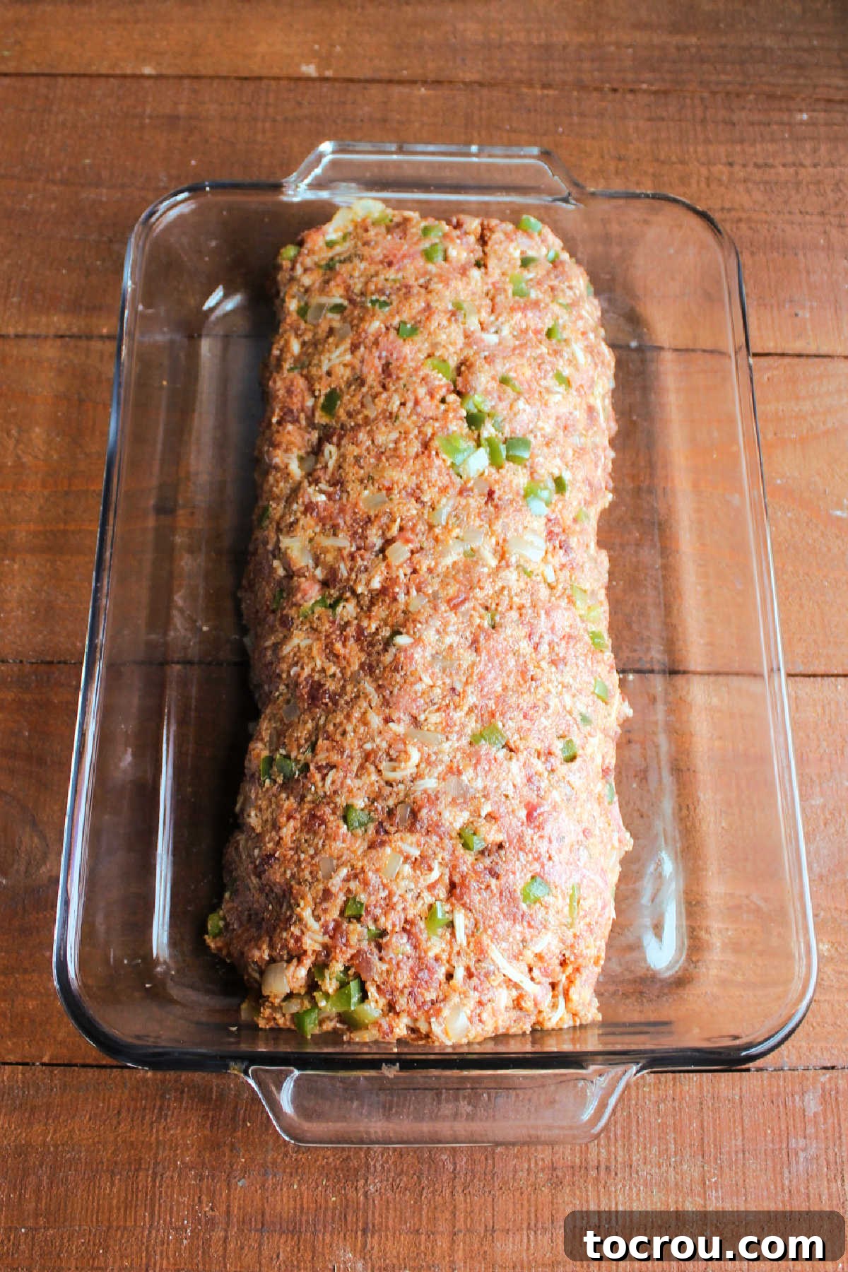 Formed meatloaf made from beef, Italian sausage, peppers, and onions shaped into a loaf in a 9x13-inch baking pan, ready for the oven.