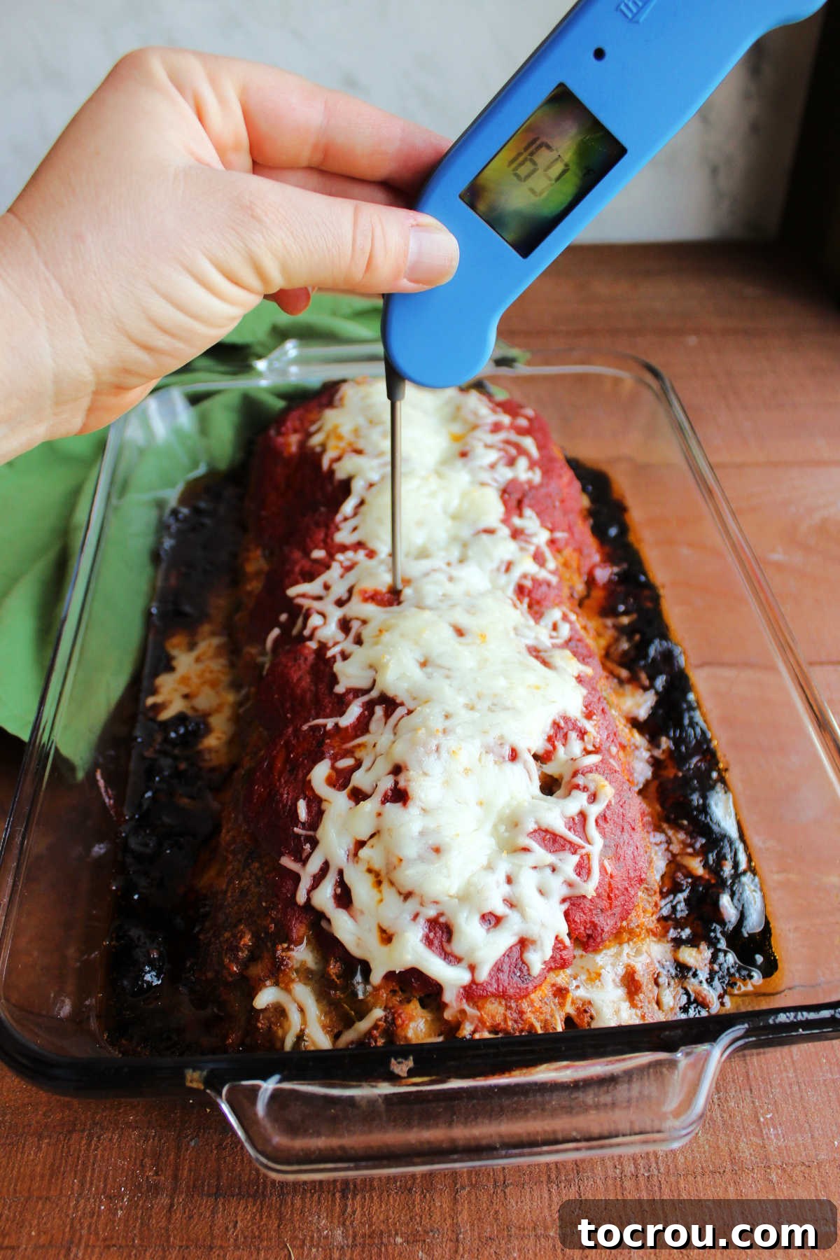 A meat thermometer inserted into a perfectly baked Italian meatloaf, topped with bubbling melted cheese, ensuring it has reached the ideal internal temperature.