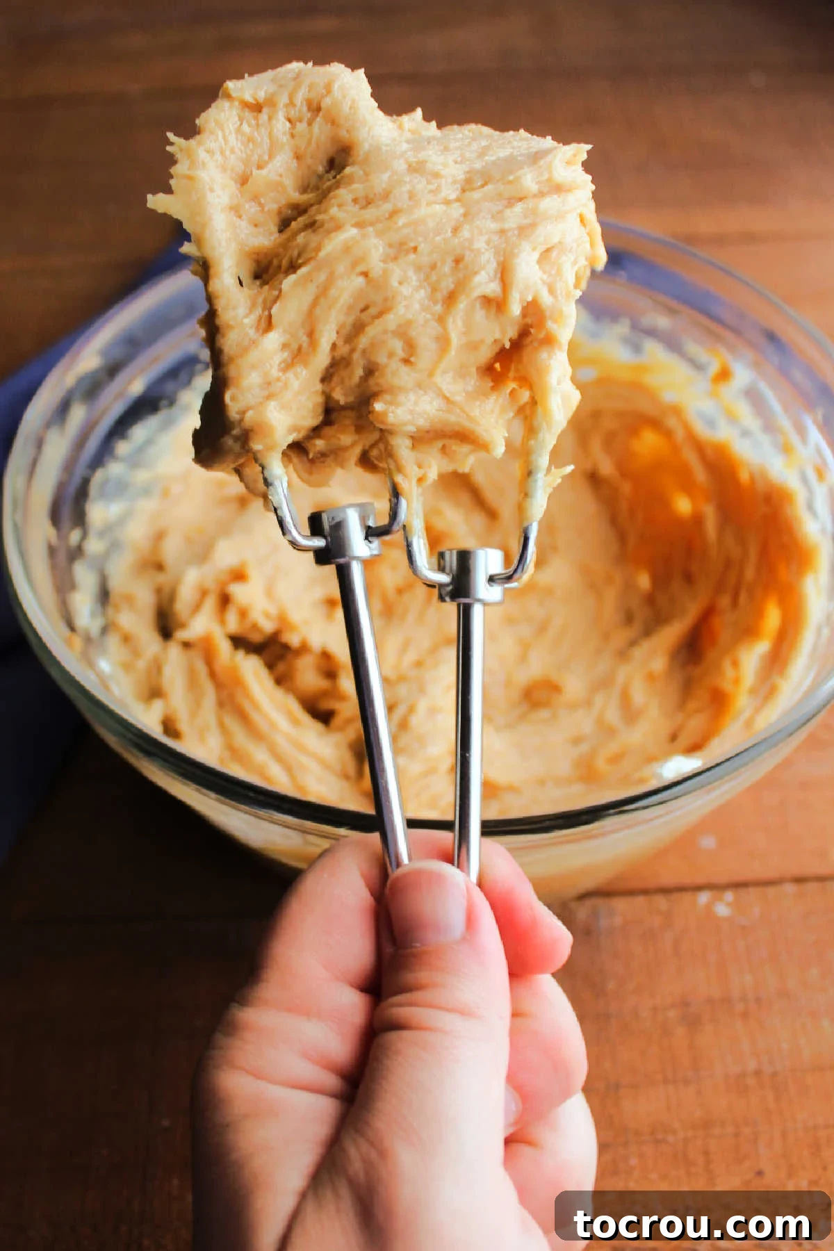 Hand holding two mixer beaters filled with peanut butter cream cheese frosting.