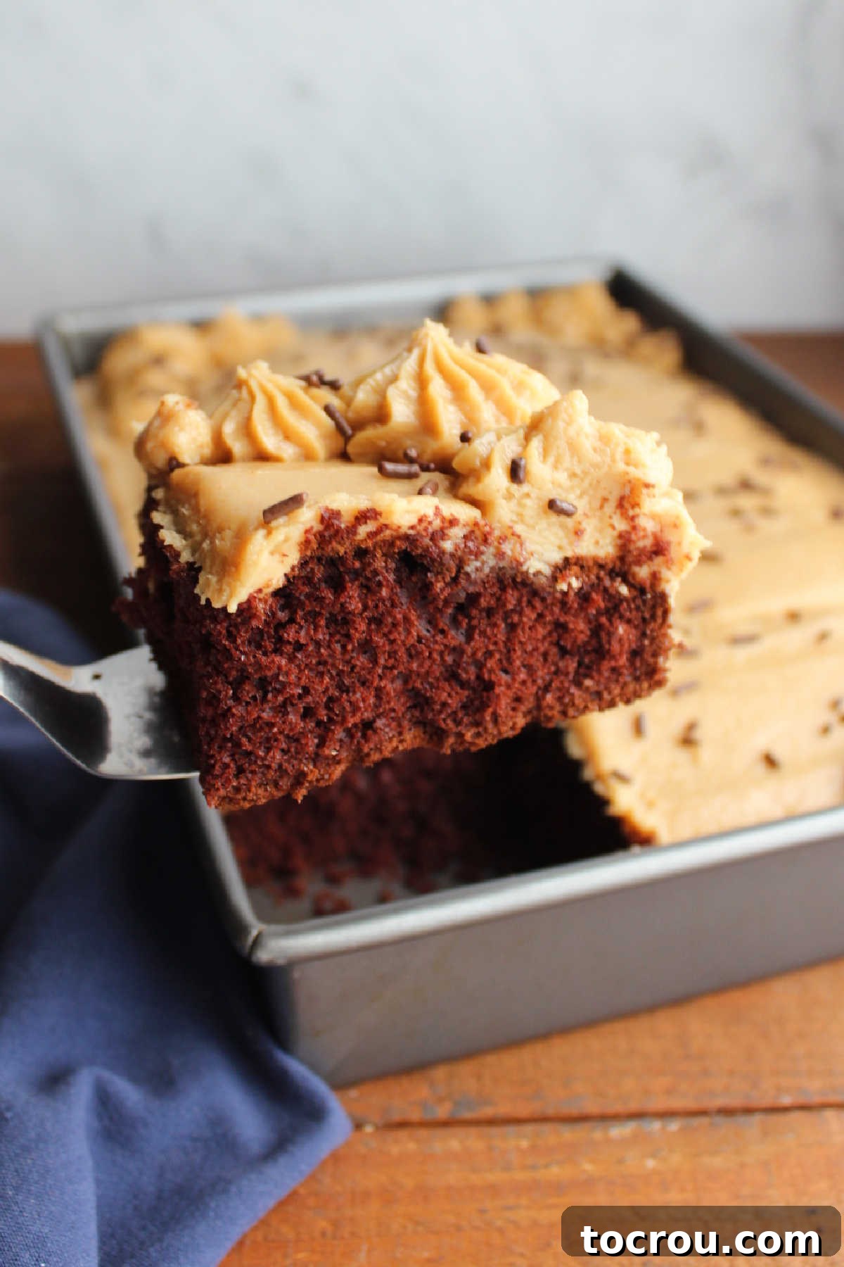 Spatula lifting a piece of cake topped with peanut butter frosting.