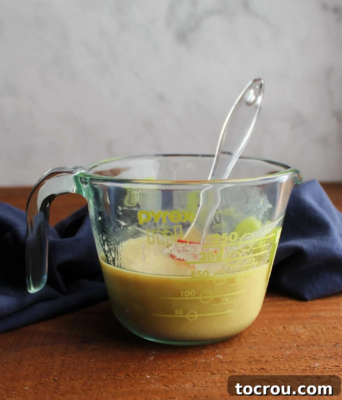 Measuring cup filled with a golden homemade peach mustard vinaigrette, ready to be used in a salad.