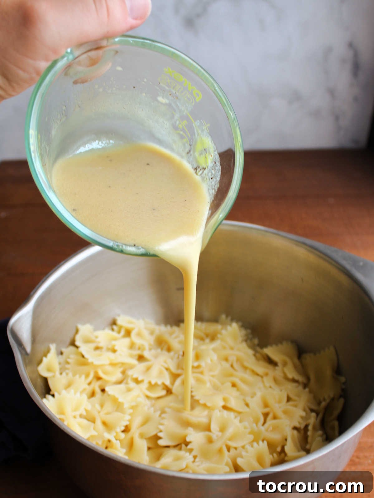Close-up shot of homemade peach mustard dressing being poured over a bowl of perfectly cooked al dente pasta.