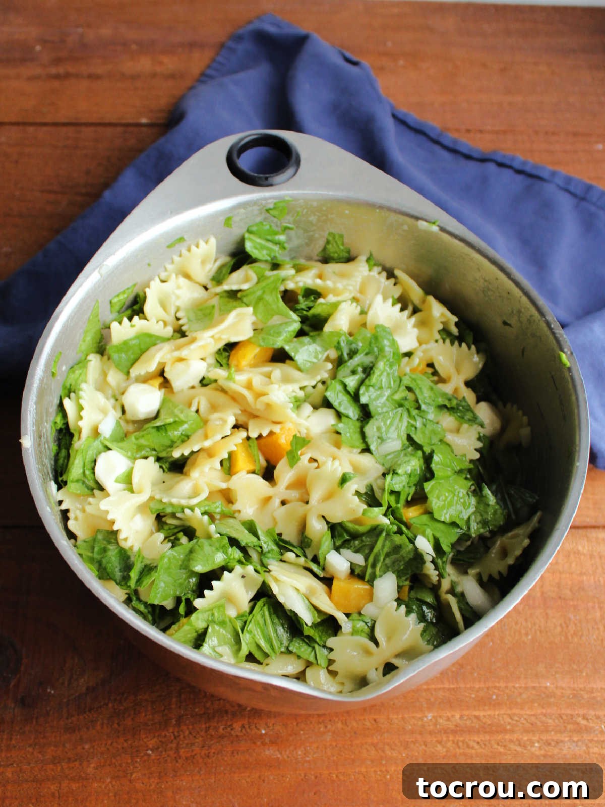 Large mixing bowl overflowing with freshly prepared peach pasta salad, featuring bright green spinach, creamy cheese, and a light dressing, ready for serving.