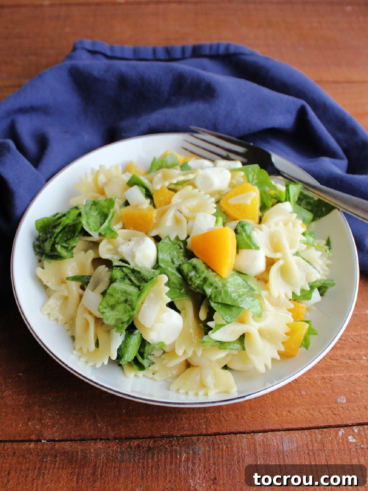 A bowl of vibrant peach pasta salad with spinach and bowtie pasta, ready to be enjoyed as a refreshing meal or side dish.